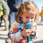 Young girl eating cupcake - face is painted around eyes with glitter facepaint