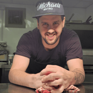 Michael patron of The Foster Care Charity in the kitchen at his bistro with his logo hat on